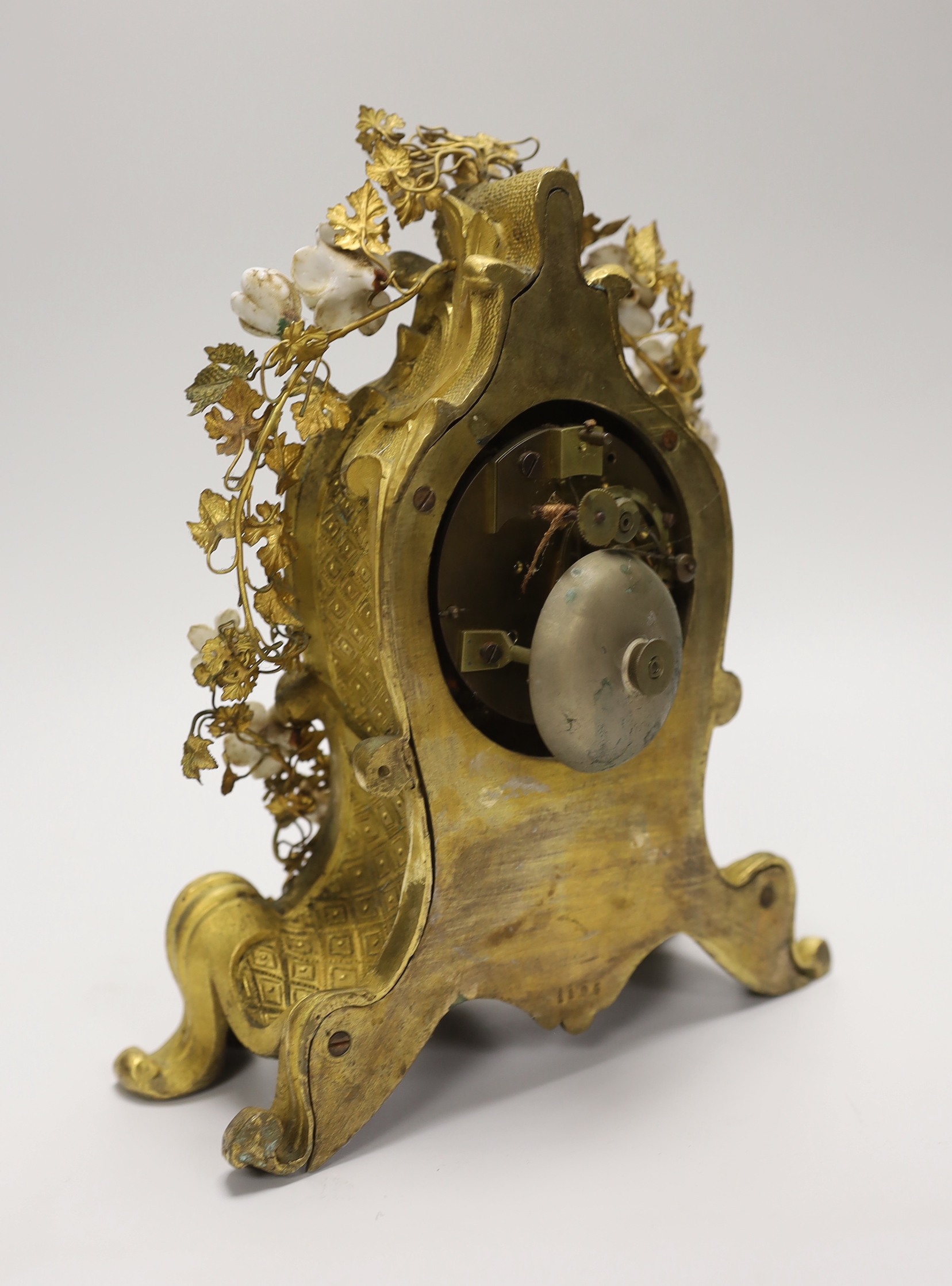 A 19th century gilt bronze and porcelain mounted mantel clock, the waisted case cast with rocaille, embellished with porcelain flower heads, with circular white enamel Roman dial, the associated twin train movement with